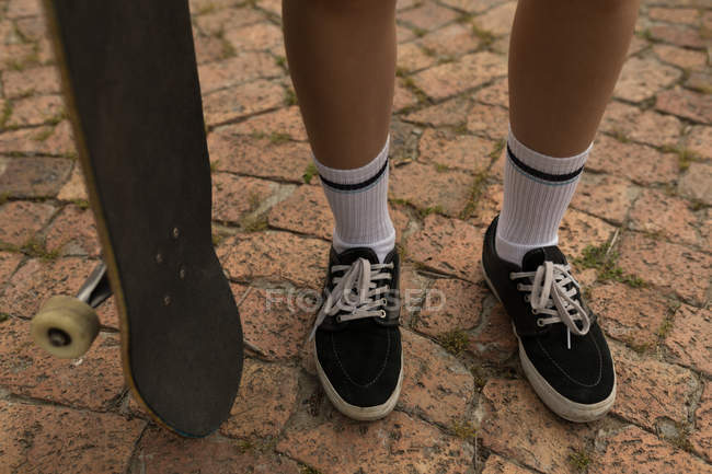 Нижняя часть скейтбордистки стоит со скейтбордом — стоковое фото