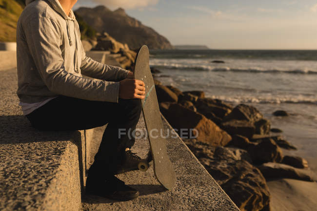 Sezione bassa di uomo seduto con skateboard sulla spiaggia — Foto stock