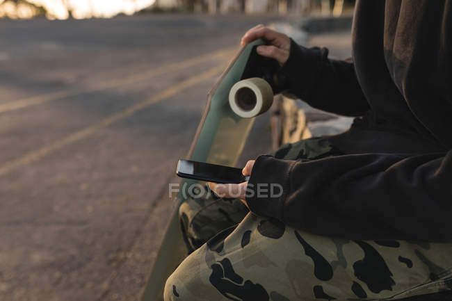 Mittelteil der Skateboarder mit Handy auf dem Land — Stockfoto