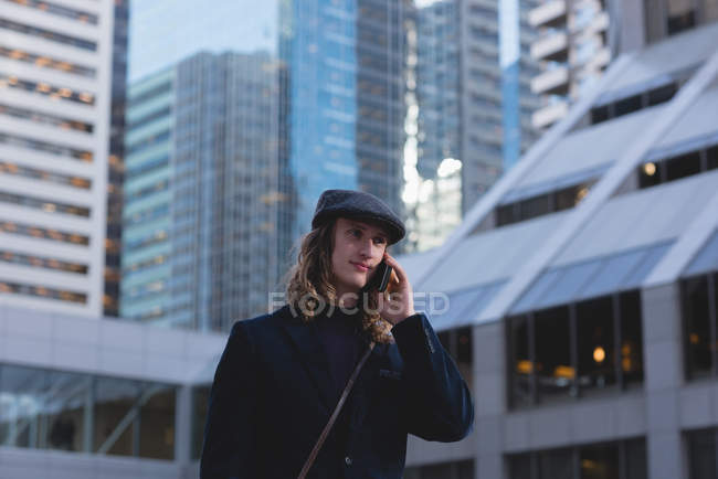Человек разговаривает по мобильному телефону во время прогулки по улице в городе — стоковое фото