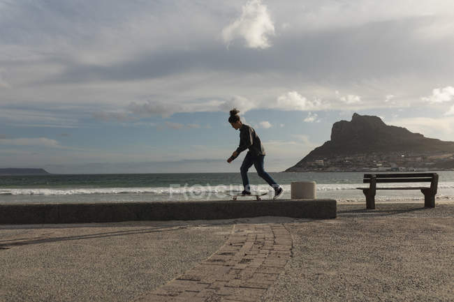 Вид сбоку человека, катающегося на скейтборде на стене у пляжа — стоковое фото