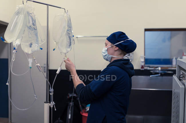 Cirujano femenino revisando gota de solución salina intravenosa en hospital - foto de stock