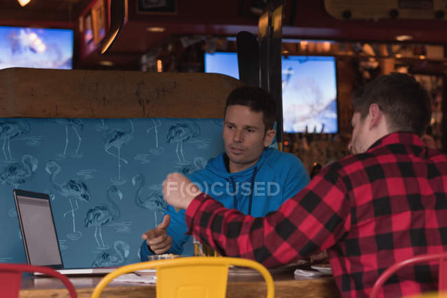 Amigos discutiendo sobre el ordenador portátil mientras toman bebidas en el pub - foto de stock