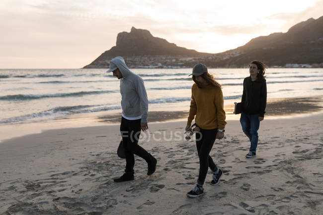 Young skateboarders walking on the beach during sunset — Stock Photo