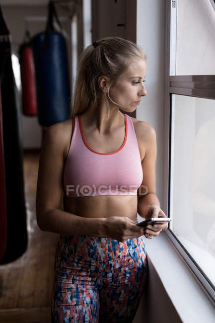 Pensativo boxeador femenino usando el teléfono móvil en el gimnasio - foto de stock
