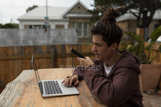 Молодий чоловік скейтбордист розмовляє на мобільному телефоні під час використання ноутбука — стокове фото