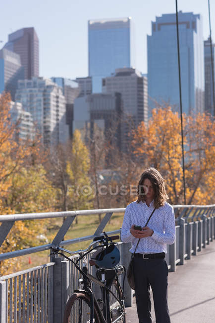 Man using mobile phone while standing with bicycle on the bridge in the city — Stock Photo