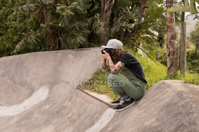 Vue latérale de la femme en cliquant sur la photo avec appareil photo numérique au parc de skateboard — Photo de stock
