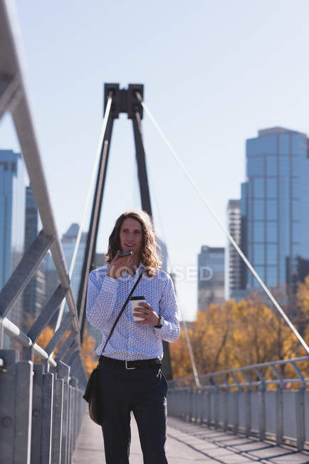 Чоловік розмовляє по мобільному телефону, маючи каву на мосту в місті — стокове фото