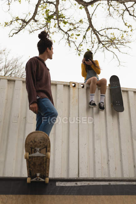 Young female skateboarder clicking photo while male skateboarder skating on skateboard ramp — Stock Photo