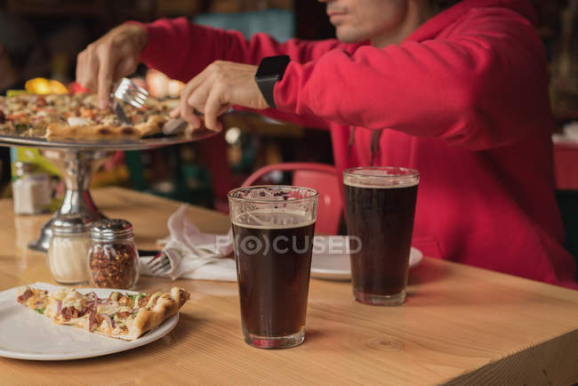 Man taking slice of pizza from tray in pub — Stock Photo
