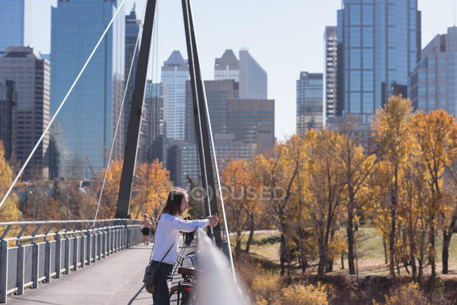 Homem atencioso de pé com bicicleta na ponte da cidade — Fotografia de Stock