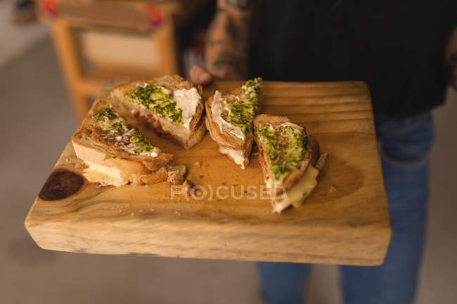 Close-up of woman holding sandwiches on wooden board — Stock Photo