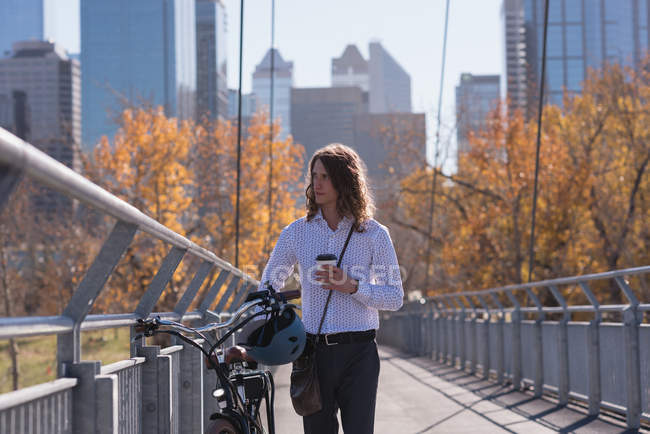Человек с помощью мобильного телефона во время прогулки на велосипеде по мосту в городе — стоковое фото