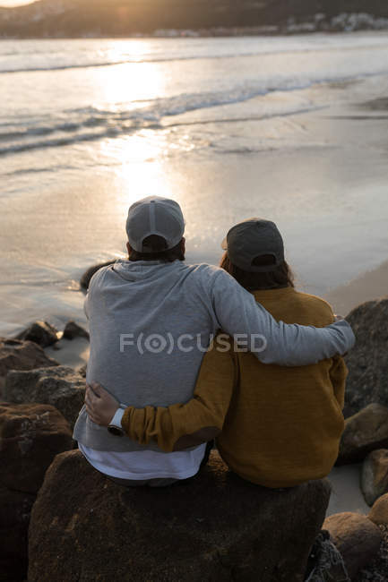 Vue arrière du couple assis sur le rocher près de la plage — Photo de stock