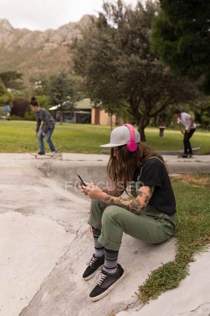 Женщина слушает музыку на мобильном телефоне в скейтборд-парке — стоковое фото