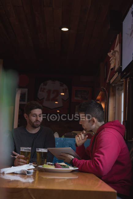 Young friends discussing over digital tablet in pub — Stock Photo