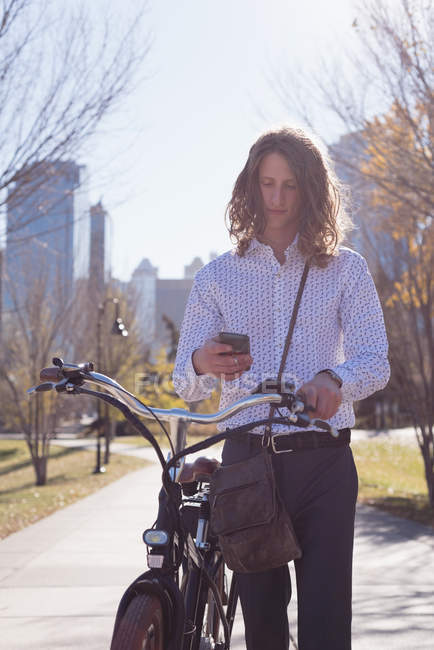 Человек с помощью мобильного телефона во время прогулки на велосипеде по улице в городе — стоковое фото
