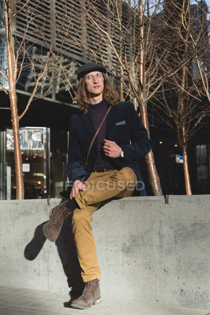 Young man relaxing on surrounding wall in the city — Stock Photo