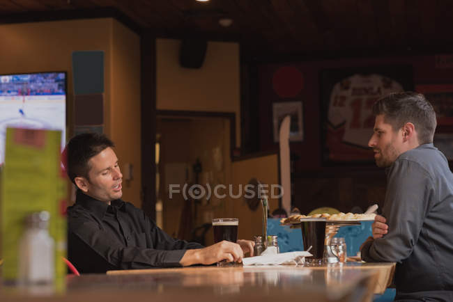 Friends talking with each other while having drinks in pub — Stock Photo