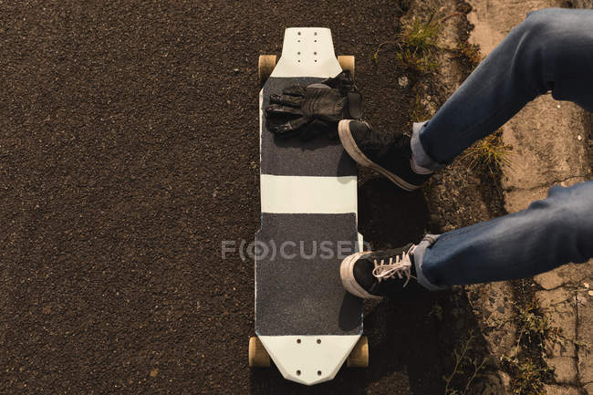 Low section of skateboarder sitting with skateboard and skateboard gloves — Stock Photo