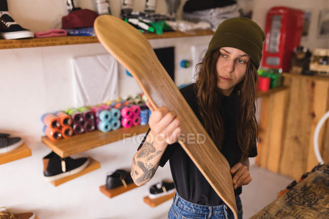 Beautiful woman examining skateboard deck in workshop — Stock Photo