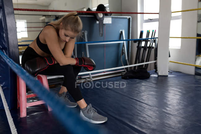 Boxer féminin fatigué se relaxant dans le ring de boxe à la salle de fitness — Photo de stock