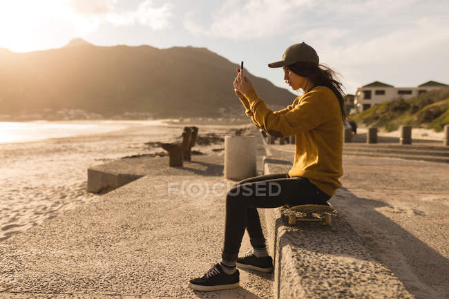 Vista lateral de la mujer haciendo clic en la foto con el teléfono móvil cerca de la playa - foto de stock