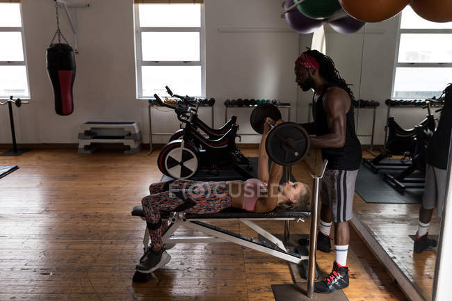Treinador masculino assistindo boxeador feminino no levantamento de barra no estúdio de fitness — Fotografia de Stock