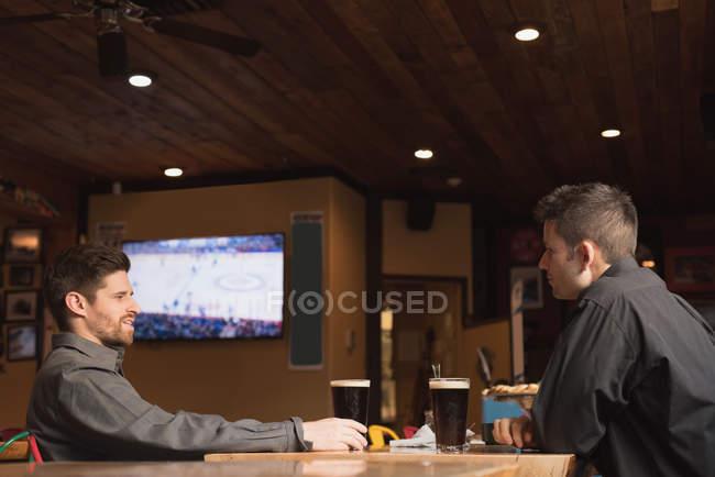Amigos hablando entre sí mientras toman bebidas en el pub - foto de stock