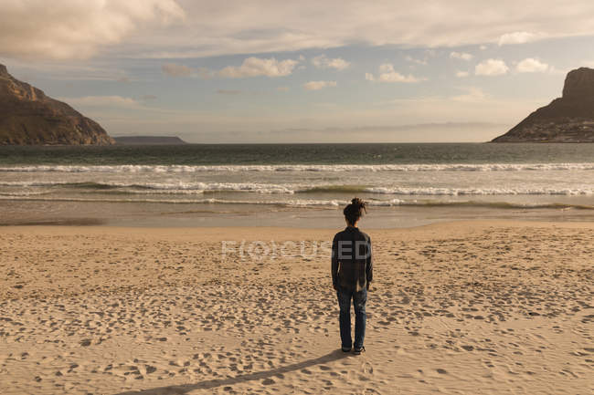 Vista trasera del hombre de pie en la playa en un día soleado - foto de stock