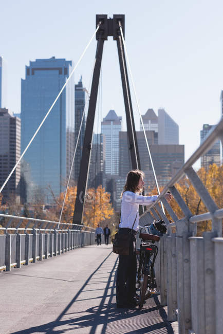 Thoughtful man standing with bicycle on the bridge in the city — Stock Photo
