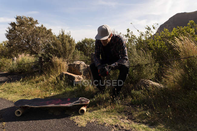 Jeune skateboarder masculin assis à la campagne — Photo de stock