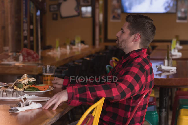 Jeune homme assis à la table avec des boissons au pub — Photo de stock