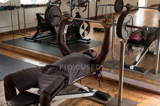 Young male boxer exercising with bench press barbell in fitness studio — Stock Photo