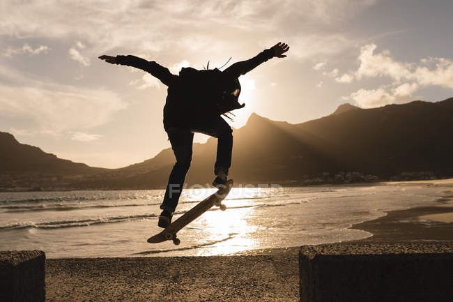 Silhouette of woman skateboarding on wall at beach — Stock Photo
