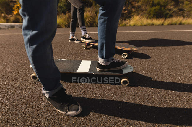 Unterteil der Skateboarder, die mit Skateboard auf der Abfahrt im Grünen stehen — Stockfoto