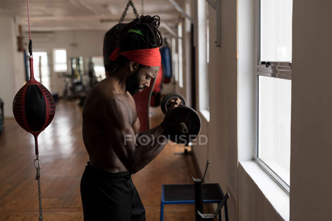Vista lateral del boxeador masculino haciendo ejercicio con barra de pesas en el gimnasio - foto de stock
