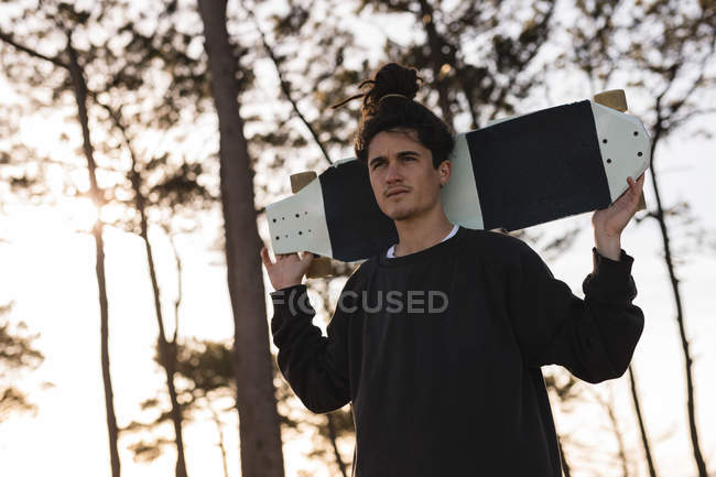 Junger männlicher Skateboarder trägt Skateboard auf Schultern — Stockfoto