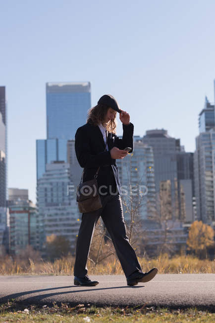 Homme utilisant un téléphone portable tout en marchant sur une route dans la ville — Photo de stock