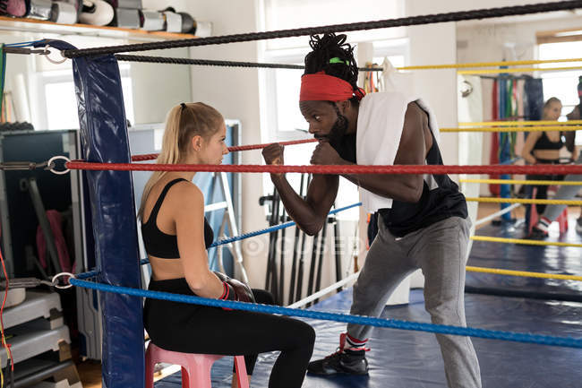 Treinador masculino assistindo boxeador feminino no ringue de boxe no estúdio de fitness — Fotografia de Stock