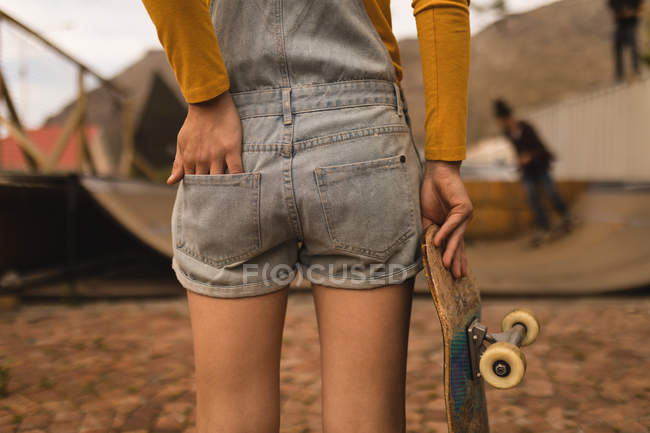 Partie médiane du skateboarder féminin debout avec skateboard — Photo de stock