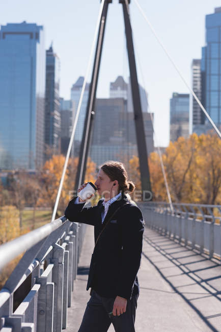 Вдумчивый человек пьет кофе на мосту в городе — стоковое фото