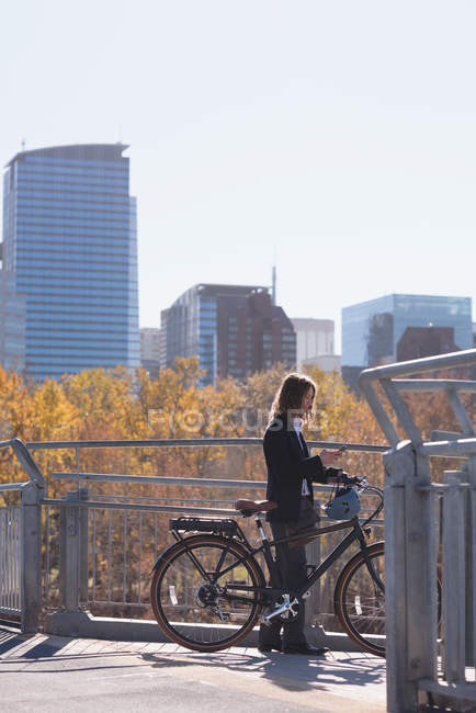 Young man standing with bicycle on the bridge in the city — Stock Photo