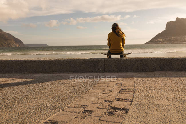 Вид сзади женщины, сидящей на скейтборде на пляже — стоковое фото