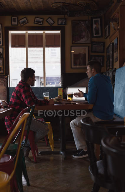 Freunde diskutieren bei Drinks in Kneipe über Laptop — Stockfoto