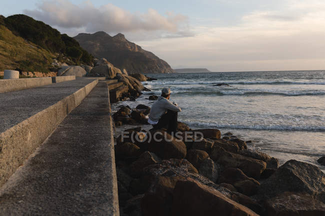 Seitenansicht eines Mannes, der bei Sonnenuntergang am Strand sitzt — Stockfoto