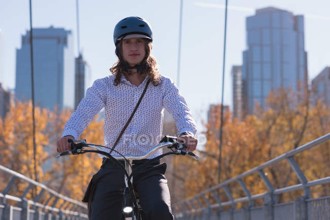 Young man riding cycle on the bridge in the city — Stock Photo