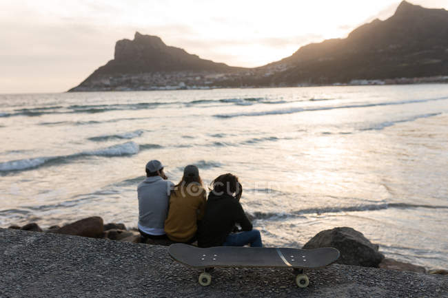 Вид сзади скейтбордистов, сидящих на пляже — стоковое фото