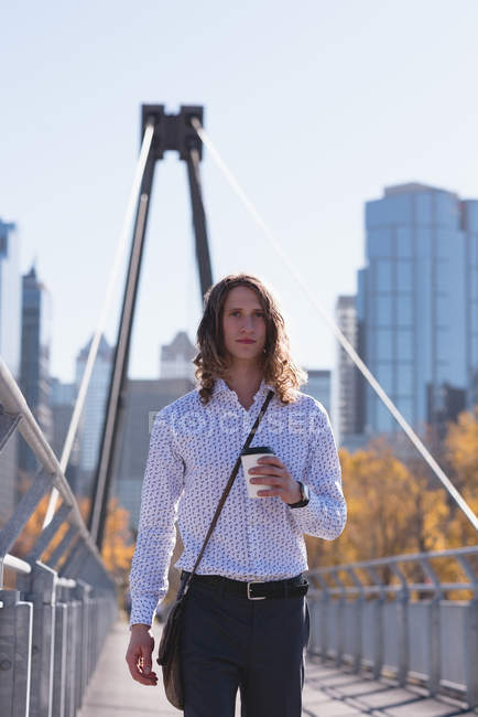 Young man holding coffee cup on the bridge in the city — Stock Photo